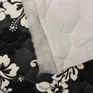 May include: Close-up of two fabric swatches. One is a black and white floral print, the other is a white quilted fabric. The floral fabric has a dark gray background with white hibiscus flowers.