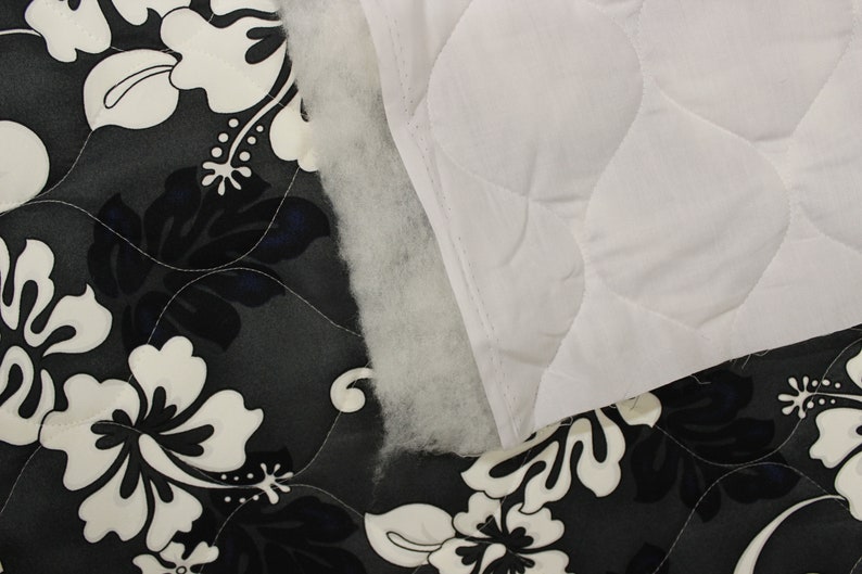May include: Close-up of two fabric swatches. One is a black and white floral print, the other is a white quilted fabric. The floral fabric has a dark gray background with white hibiscus flowers.
