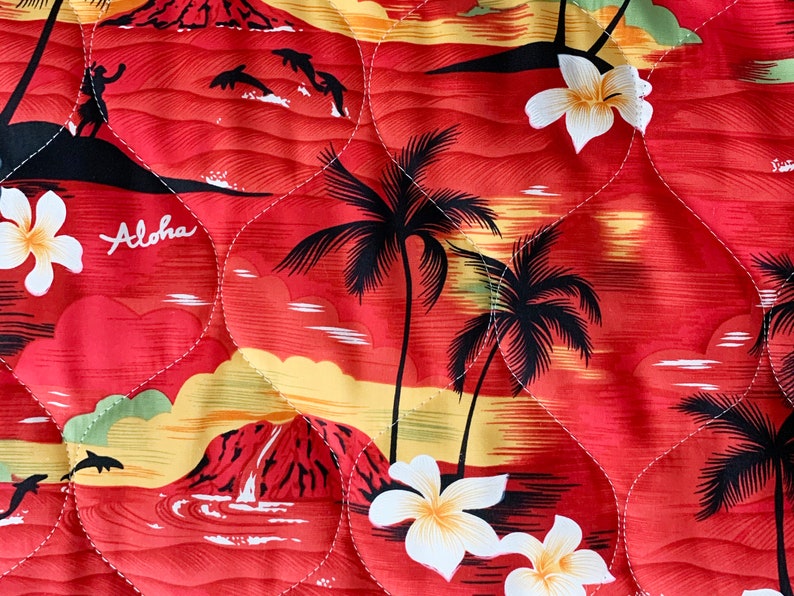 May include: Red fabric with a quilted pattern featuring a tropical sunset scene with palm trees, white flowers, and the word "Aloha".