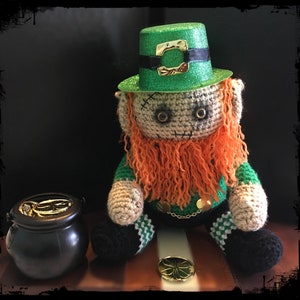 May include: A crocheted leprechaun doll wearing a green glitter hat with a gold buckle. The doll is holding a pot of gold coins and has a long orange beard.
