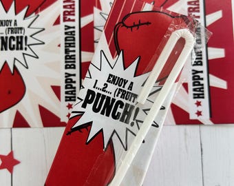 May include: Red and white birthday-themed party favor bags with a boxing glove design. The bags have the text "HAPPY BIRTHDAY FRANKIE!" and "ENJOY A...PUNCH!" printed on them. A white straw is visible in a clear plastic wrapper.