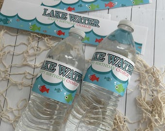 May include: Two clear plastic water bottles with labels that read "Lake Water Happy Birthday Charlie". The labels feature a blue wave design with red and green fish. Decorative fishing net is in the background.