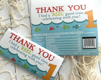 May include: A white candy bar wrapper and a card with a blue ocean theme. The text reads "THANK YOU, I had a 'REEL' good time, celebrating with you!" with a number one and fish illustrations. The card has a nutrition facts table.