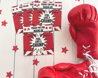 May include: Red boxing gloves and cards with a boxing glove graphic and the text "THANK YOU FOR MAKING ME FEEL LIKE A CHAMP!". Red star-shaped confetti is scattered around the gloves and cards on a white wooden surface.