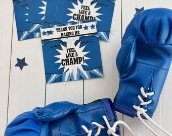 May include: Blue boxing gloves with white laces and several blue cards. The cards have the text "THANK YOU FOR MAKING ME" and "FEEL LIKE A CHAMP!" with star accents. The background has star decorations.