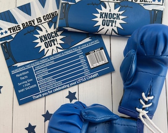 May include: Blue boxing gloves and baby shower favors with the text "This Baby Is Going To Be..." and "Knock Out!". The favors list ingredients like happiness and laughter. The theme is a baby shower.