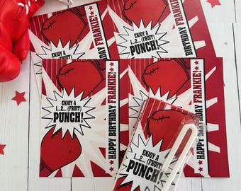May include: Red boxing gloves and birthday-themed juice boxes with the text "Enjoy a 1...2... (Fruit) Punch!" and "Happy Birthday Frankie!" on a white wooden surface. Red star-shaped confetti is scattered around.