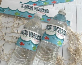 May include: Two clear plastic water bottles with labels that read "Lake Water Happy Birthday Charlie". The labels have a blue wave design with red and green fish. Decorative fishing net is in the background.