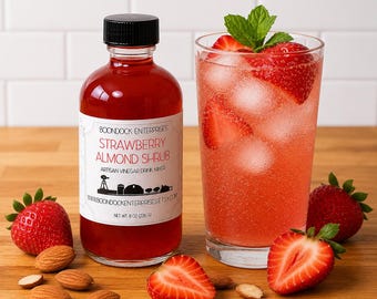 May include: A glass bottle of Boondock Enterprises Strawberry Almond Shrub artisan vinegar drink mixer, net weight 8 oz (226 g), next to a glass of pink strawberry drink with ice, mint leaves, and scattered whole and sliced strawberries and almonds.