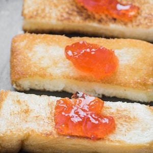Puede incluir: Tres rebanadas rectangulares de pan tostado dorado dispuestas en fila. Cada rebanada de pan tiene una porci&oacute;n de mermelada de frutas de color naranja brillante, con una superficie brillante, texturizada y de aspecto ligeramente transl&uacute;cido.