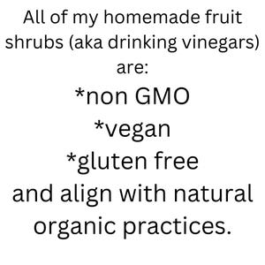 Op de afbeelding: Tekst op een witte achtergrond die aangeeft dat alle zelfgemaakte fruitshrubs (ook wel drinkazijn genoemd) niet-GMO, veganistisch, glutenvrij zijn en in lijn zijn met natuurlijke biologische praktijken.