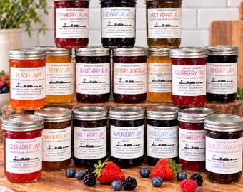 May include: A collection of eighteen glass jars filled with various fruit jams and jellies, each featuring a white label with black text. The jars are arranged in rows on a wooden surface, accompanied by fresh strawberries and blueberries.