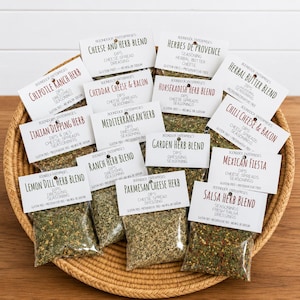 May include: A woven basket holds several small packets of herbs and seasonings. Each packet has a white label with the product name, such as "Chipotle Ranch Herb" and "Cheese and Herb Blend." The labels also list the product's uses, like dips and dressings.