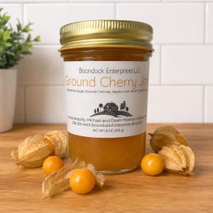 May include: A glass jar of Boondock Enterprises LLC Ground Cherry Jam with a gold lid. The white label lists ingredients including sugar, ground cherries, apple juice, pectin, and lemon juice, with a net weight of 8 oz (226 g) and fresh ground cherries.