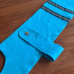 May include: A light blue felt dog vest with a reflective strip and a button closure.