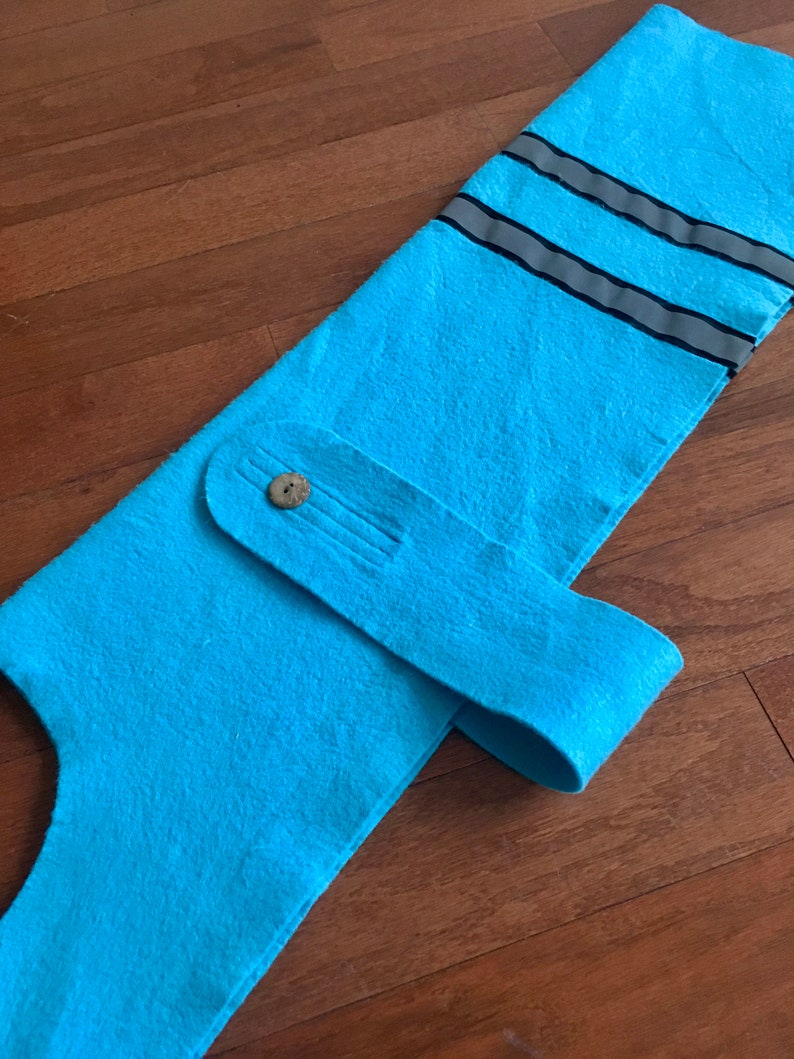 May include: A light blue felt dog vest with a reflective strip and a button closure.