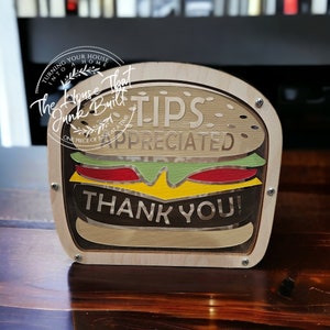 May include: Wooden burger-shaped tip jar with the text "Tips Appreciated" and "Thank You!" on it.