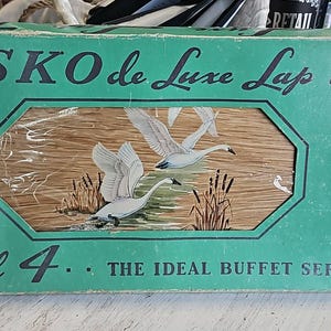 May include: Vintage HASKO de Luxe Lap Trays box set of 4. The box is teal with the text "HASKO de Luxe Lap Trays" and "Set of 4". The center of the box features a picture of swans in a marsh. The text "THE IDEAL BUFFET SERVICE" is at the bottom.