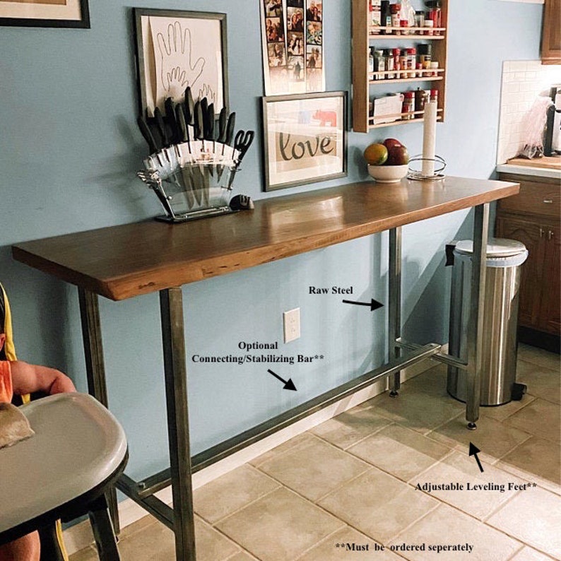 Puede incluir: Una barra de mostrador de madera r&uacute;stica con patas de acero en bruto y patas niveladoras ajustables. La barra se muestra en un entorno de cocina con una pared azul y un salpicadero de azulejos blancos. La barra tiene 76 cm (30 pulgadas) de alto y tiene una barra de conexi&oacute;n/estabilizaci&oacute;n que se puede pedir por separado.