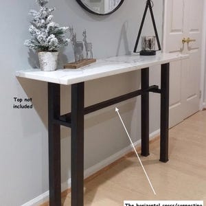 May include: A black metal console table base featuring four vertical legs and a horizontal connecting bar. The text 'Top not included' is visible on the left, and 'The horizontal cross/connecting bar can be ordered in various lengths in our separate listing' is printed below.