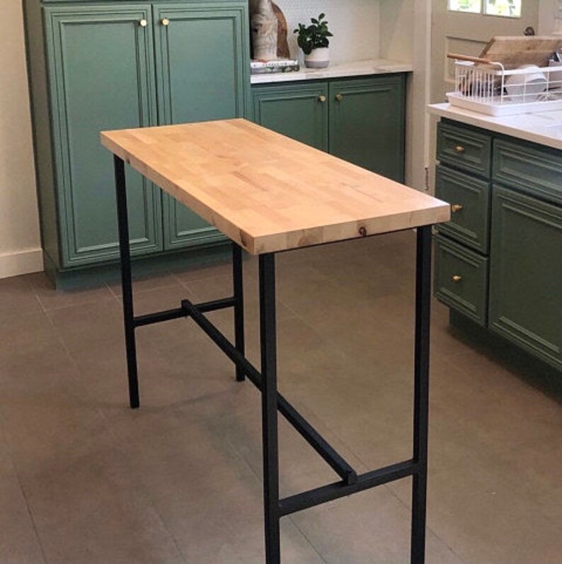 Puede incluir: Una mesa de bar de encimera de madera con un marco de metal negro. La mesa tiene una tapa rectangular y un dise&ntilde;o sencillo.