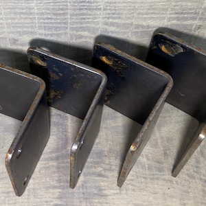 May include: Four black metal brackets with a 90-degree angle. The brackets are made of sturdy metal and have a rustic finish.