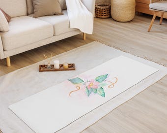 May include: White yoga mat with a watercolor floral design featuring a pink flower and green leaves. The mat is on a light brown wooden floor.