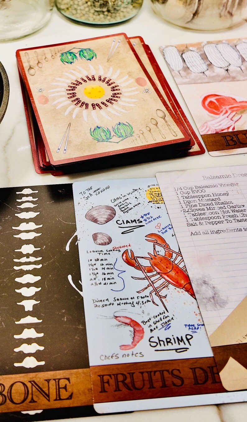 May include: A stack of recipe cards with a floral design and handwritten notes. One card features a lobster illustration and the word "Shrimp." Other cards show recipes and cooking times. The cards have red edges.