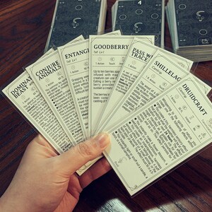 May include: A spread of cards featuring various spells and abilities for a fantasy role-playing game. The cards are printed with black text on a white background and feature illustrations of nature and magical elements. The cards include spells like "Dominate Beast", "Conjure Animals", "Entangle", "Goodberry", "Pass Without Trace", "Shillelagh", and "Druidcraft".