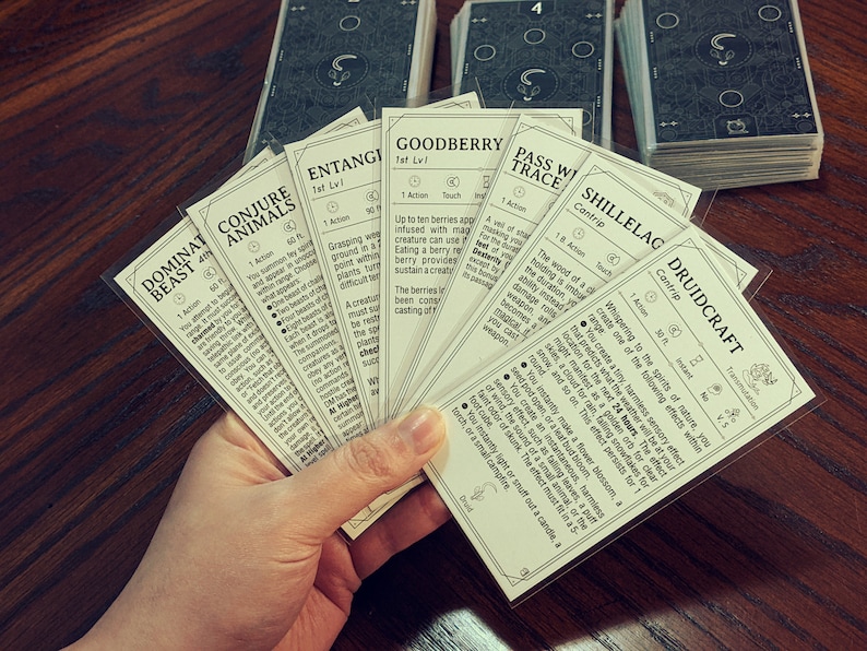 May include: A spread of cards featuring various spells and abilities for a fantasy role-playing game. The cards are printed with black text on a white background and feature illustrations of nature and magical elements. The cards include spells like "Dominate Beast", "Conjure Animals", "Entangle", "Goodberry", "Pass Without Trace", "Shillelagh", and "Druidcraft".