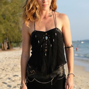 May include: A woman wearing a black top with a beaded design and a black mesh skirt. She is standing on a sandy beach.