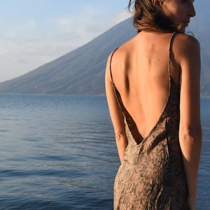 Puede incluir: Vestido con estampado de piel de serpiente marrón y verde, con tirantes finos y espalda baja. El vestido llega a la rodilla y tiene un dobladillo ligeramente asimétrico. El fondo presenta un lago y una montaña.