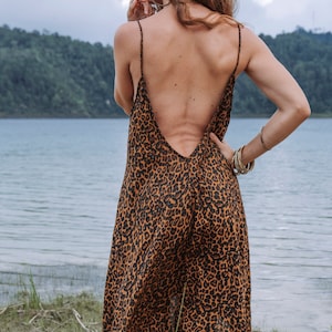 Modèle portant une robe à bretelles mi-longue imprimé léopard marron, vue de dos, dos-nu plongeant. Décor au bord d'un lac, ciel nuageux.