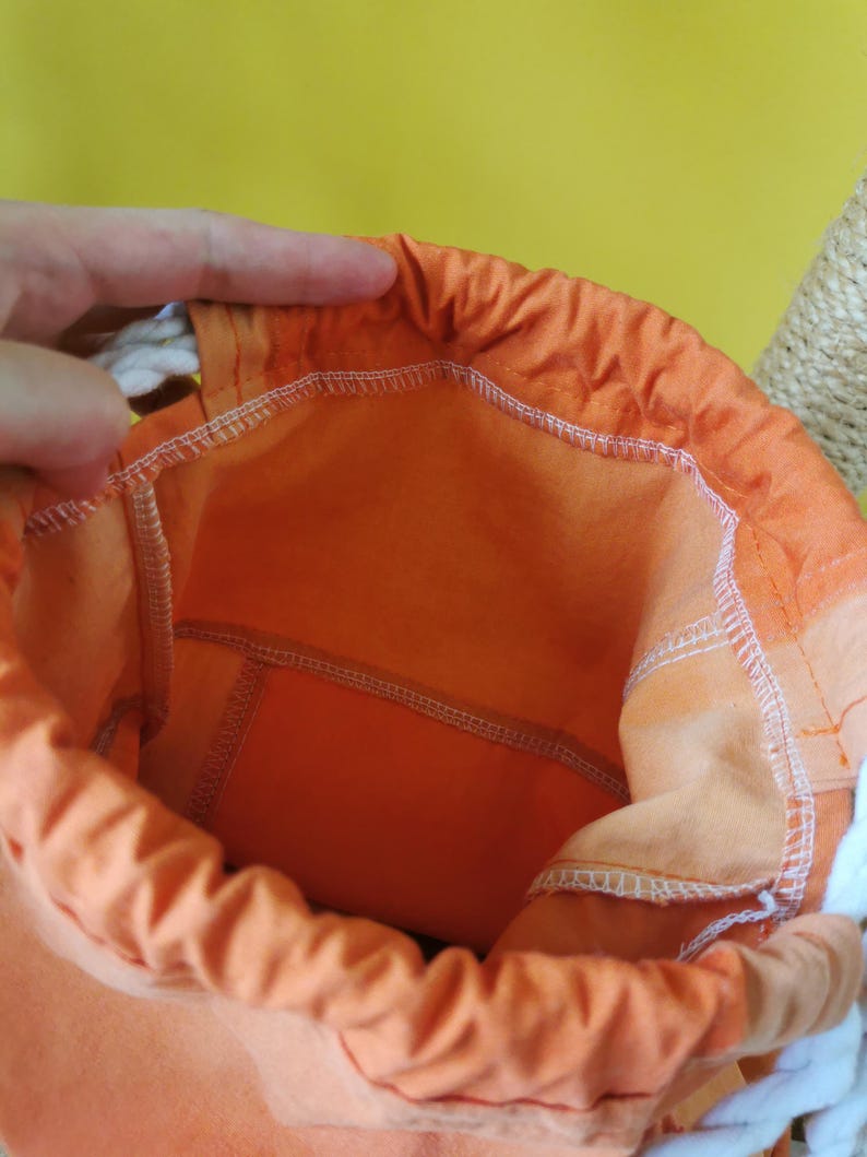 K&ouml;nnte beinhalten: Ein offener orangefarbener Beutel mit wei&szlig;em Kordelzug. Die Innenseite des Beutels ist in einem helleren Orangeton gehalten. Der Beutel besteht aus einem weichen Stoff und hat wei&szlig;e N&auml;hte.