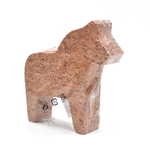 Puede incluir: Una figurita de caballo Dala de corcho marrón. La figurita está hecha de corcho y tiene un aspecto natural y rústico. La figurita está envuelta en plástico y tiene un símbolo de reciclaje en la parte inferior.