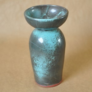 Peut inclure: Un vase en céramique fait à la main avec un design unique. Le vase présente une base gris foncé avec des accents turquoise et un petit dessus en forme de bol. La base a une texture craquelée et un bord rouge. Le vase mesure environ 18 cm de haut.
