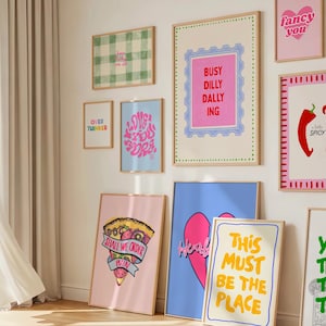 May include: A gallery wall featuring multiple framed art prints with colorful graphic designs and text. Prints include phrases like 'Busy Dilly Dallying', 'I Love You More', 'Shall We Order Pizza?', 'Fancy You', 'A Little Spicy', and 'This Must Be The Place'.