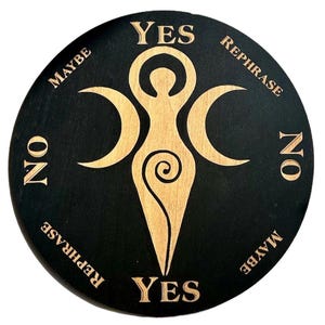 Puede incluir: Un tablero de adivinación redondo de madera negra con texto y diseño grabados en color dorado. El diseño presenta una figura central con lunas crecientes y las palabras "YES", "NO", "MAYBE" y "REPHRASE".