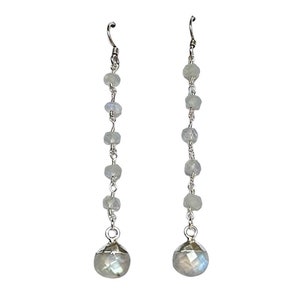 May include: A pair of long silver dangle earrings with a silver hook and a large round moonstone at the bottom. The earrings are made with a chain of smaller moonstone beads.