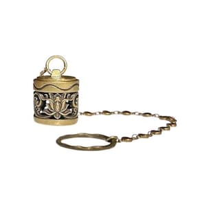 May include: A cylindrical brass-toned metal pendant featuring an intricate openwork lotus flower design. The top has a small loop, and a delicate chain connects the pendant to a larger, textured circular ring, creating a cohesive metal accessory.