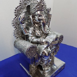 Puede incluir: Estatua de Ganesha, el dios hind&uacute; de la sabidur&iacute;a y la prosperidad, en plata plateada, sentado en un trono con intrincados detalles. La estatua est&aacute; altamente pulida y tiene una superficie reflectante.