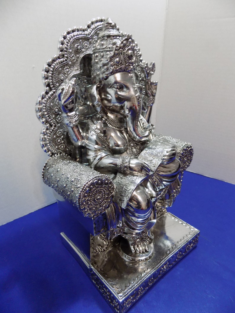 Puede incluir: Estatua de Ganesha, el dios hind&uacute; de la sabidur&iacute;a y la prosperidad, en plata plateada, sentado en un trono con intrincados detalles. La estatua est&aacute; altamente pulida y tiene una superficie reflectante.