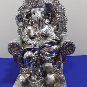 Puede incluir: Estatua de plata de Ganesha, el dios hind&uacute; de la sabidur&iacute;a y la prosperidad, sentado en un trono con intrincados detalles. La estatua est&aacute; hecha de plata pulida y tiene un dise&ntilde;o detallado.