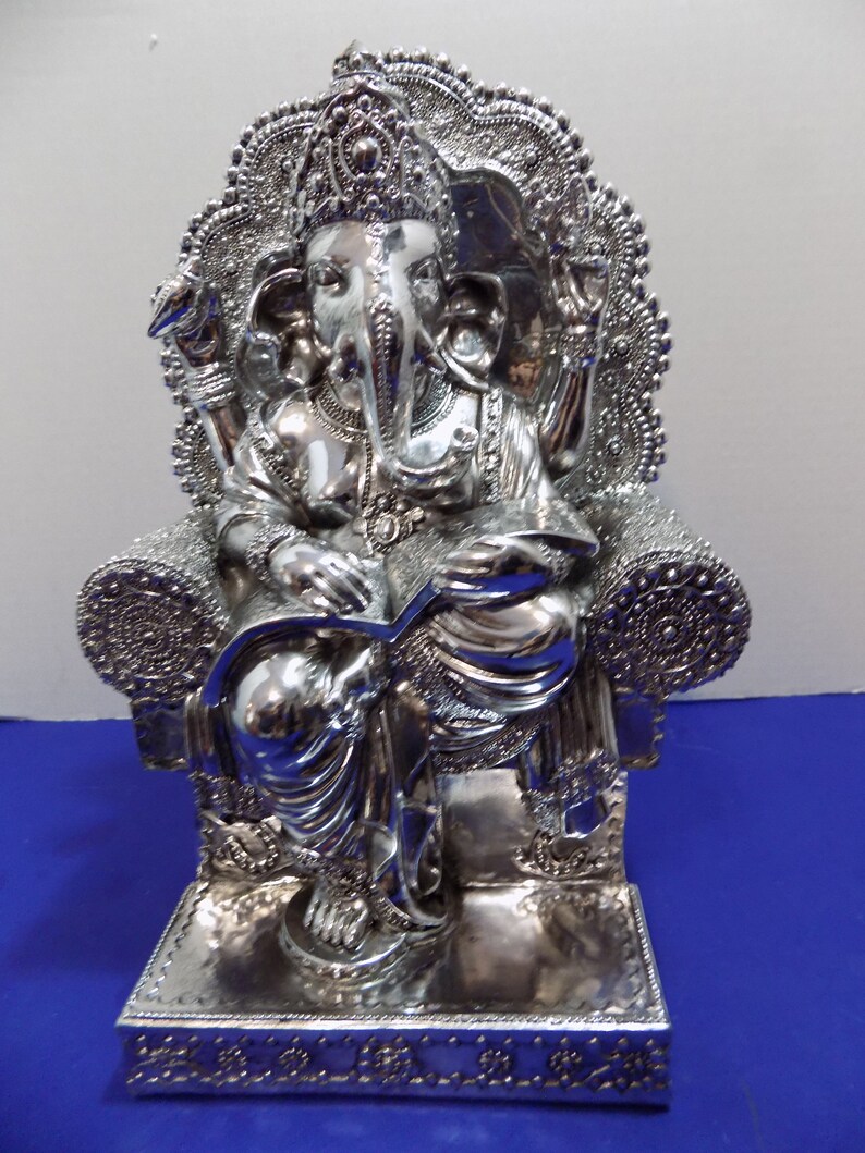 Puede incluir: Estatua de plata de Ganesha, el dios hind&uacute; de la sabidur&iacute;a y la prosperidad, sentado en un trono con intrincados detalles. La estatua est&aacute; hecha de plata pulida y tiene un dise&ntilde;o detallado.