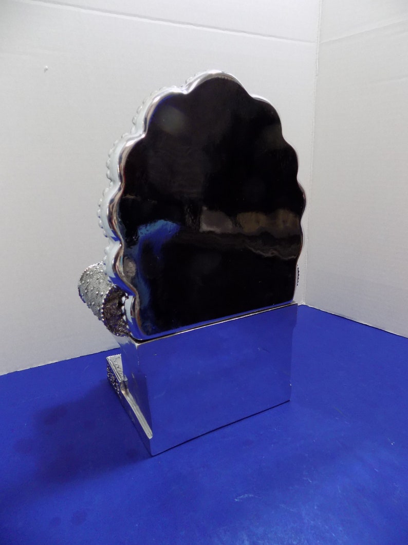 Puede incluir: Un trono de cer&aacute;mica de color plateado con un respaldo festoneado y una base rectangular. El trono est&aacute; decorado con diamantes de imitaci&oacute;n y tiene un acabado de espejo.