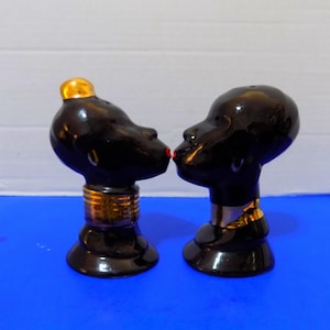 May include: A white ceramic mug with a black handle and the text "But First, Coffee" in a bold, black font. The mug is set against a blurred background, suggesting a cozy setting.