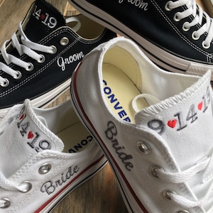 K&ouml;nnte beinhalten: Ein Paar wei&szlig;e und schwarze Canvas-Schuhe mit den Worten "Bride" und "Groom", die darauf gestickt sind. Die Schuhe haben auch das Datum "9.14" und ein Herz, das darauf gestickt ist.