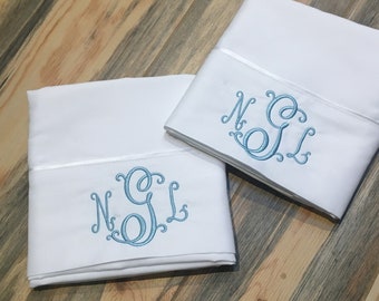 May include: Two white pillowcases with blue embroidered monograms. The monogram is "N.G.L."