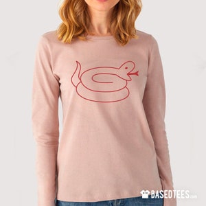 Puede incluir: Una camiseta rosa de manga larga con un contorno rojo de una serpiente enroscada con la boca abierta. La serpiente está centrada en la camiseta.