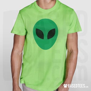 May include: A lime green t-shirt with a green alien face design and black eyes. The alien graphic is centrally placed on the front. The t-shirt has short sleeves and a crew neck.